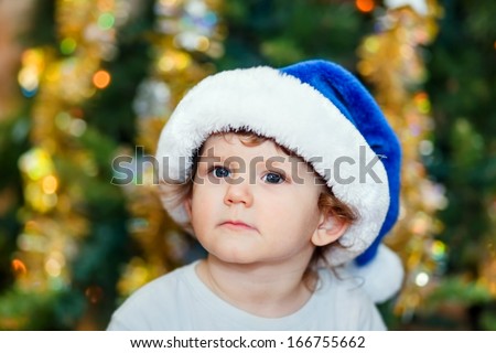 Portrait of a smart kid in a blue Santa hat, close-up on New - stock-photo-portrait-of-a-smart-kid-in-a-blue-santa-hat-close-up-on-new-year-s-background-bokeh-166755662