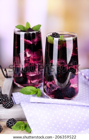 Tasty cool blackberry lemonade with ice on wooden table, on light background - stock photo