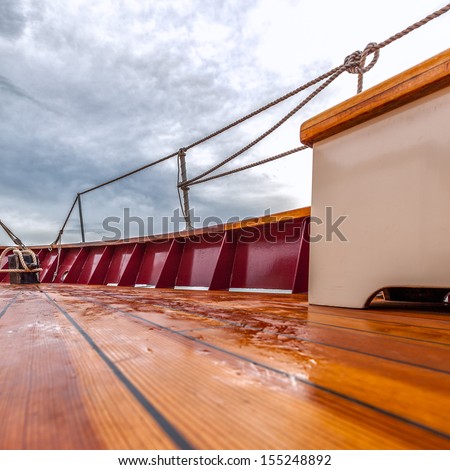 Wet wooden deck of a sailboat at sea under stormy skies. Square format 