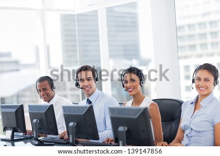 Line of call centre employees smiling and working on computers  stock 