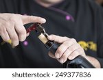Small photo of closeup of the hands of a young man uncorking a bottle of red wine with a corkscrew - focus on the mouth of the bottle