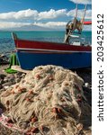 Small photo of Drift net and a fishing boat in a small harbour of the sicilian coast with clouds and Mount Etna in the background