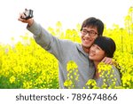 Small photo of happy young asian couple talking picture in the spring flower field