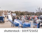 Small photo of Blurred child sliding on giant inflatable snow tube at wintertime community event in Texas, USA. People talking picture, large group of diverse multiethnic crowd family members waiting.