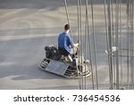 Small photo of Employee performs sand and cement screed floor with ride-on trowels with dual counter-rotating rotors "helicopters" with four blades on each rotor.