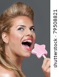 An expressive close-up portrait of an attractive blond female with a vintage hairstyle and make up, looking happy and eating a ice cream. - stock photo