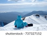 Small photo of Snowboarder sitting and looking at mountain chain in the background