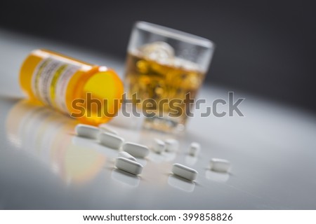 Several Prescription Drugs Spilled From Fallen Bottle Near Glass of Alcohol.