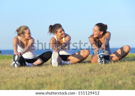 Group of three women stretching after sport on the grass with the sea in the background