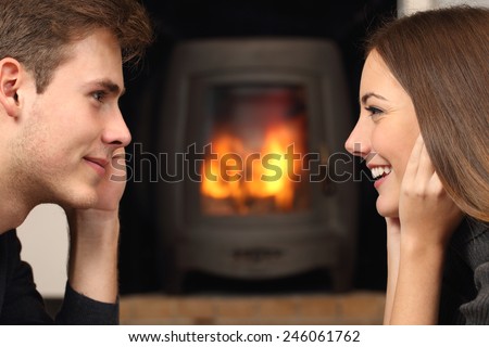 Side view of a couple flirting and looking each other in front a fireplace