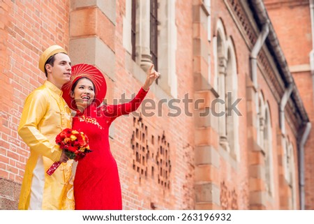 Beautiful bride in Vietnamese national costume showing something to her husband