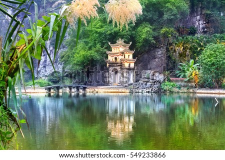 Outdoor park landscape with stone bridge and lake. Gate entrance to old Bich Dong pagoda complex. Ninh Binh, Vietnam - travel destination.