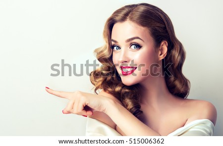 Woman surprise showing product .Beautiful girl with curly hair pointing to the side . Presenting your product. Isolated on white background. Expressive facial expressions