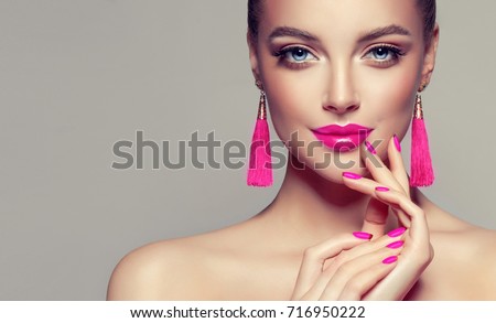 Beautiful model girl with pink fuchsia manicure on nails . Fashion makeup and cosmetics . Large earrings tassels jewelry Magenta color .