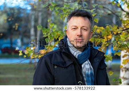 Handsome happy smiling man. Outdoor autumn male portrait. Attractive confident middle-aged man posing in city park, birch grove.