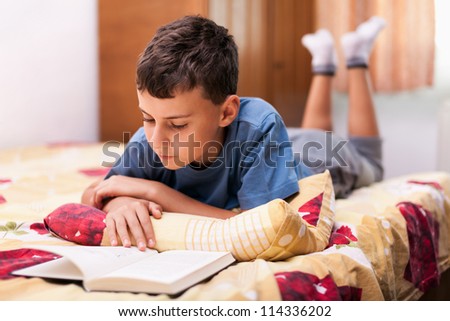Studio portrait of a schoolboy reading a textbook while lying in bed