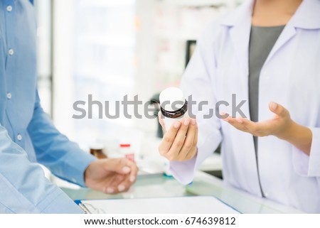 Female pharmacist holding medicine bottle giving advice to customer in chemist shop or pharmacy