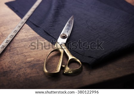 Measuring and cutting textile or fine cloth. Work table of a tailor. Gold scissors and black silky fabric. Intentionally shot in retro muted color.