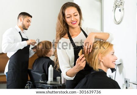 Smiling client sitting in a hair salon while hairdresser is combing her hair. Focus on client