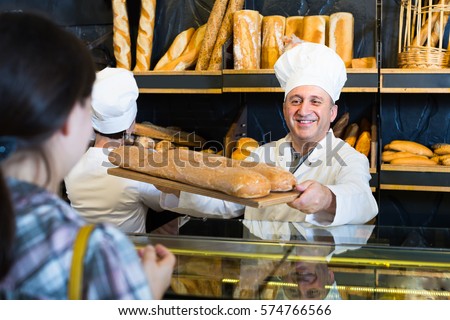 Portrait of female customer buying fresh bread from cheerful baker
