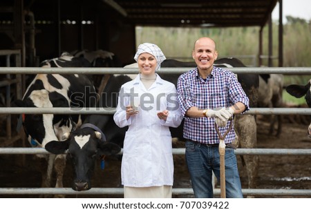 Laughing veterinarian with fresh milk chatting with farmer in hangar with cows