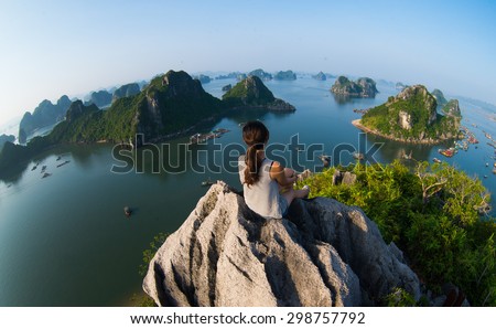 A young traveler girl sit on the top of mountain in Halong bay and enjoy the beauty of seascape. Young girl love wild life, travel, freedom.