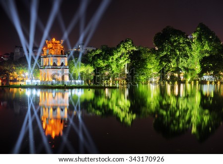 Night view of the Hoan Kiem Lake (Lake of the Returned Sword) and the Turtle Tower among blue light rays at historic centre of Hanoi in Vietnam. The tower reflected in the lake.
