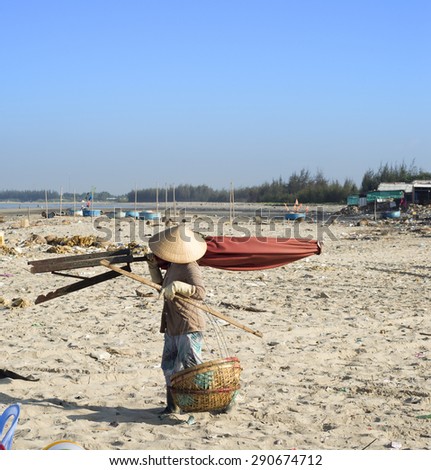 LONG HAI, VIET NAM - MAY 31 2015: A woman carrying umberlla and fish baskets at the early morning market. This is their daily life