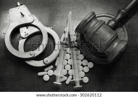 Judge's gavel with handcuffs, drugs and syringes on wooden table, drugs concept
