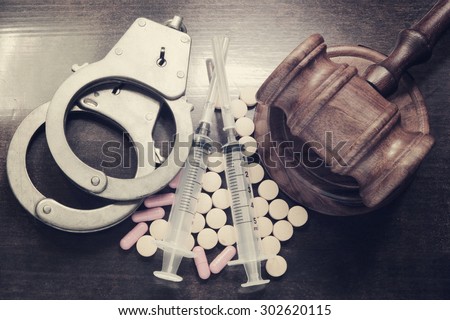 Judge's gavel with handcuffs, drugs and syringes on wooden table, drugs concept