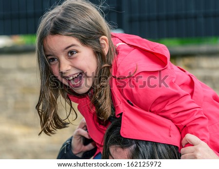 pretty laughing child perched on the shoulder of her mother
