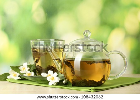 green tea with jasmine in cup and teapot on wooden table on green background