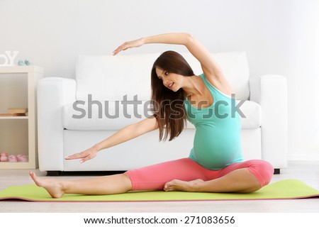 Pregnant woman exercising on green mat in room