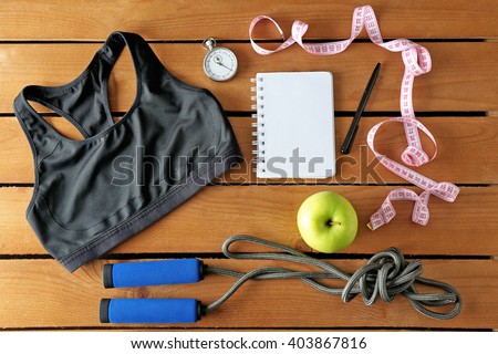 Athlete's set with female clothing, equipment, apple and notebook on wooden background