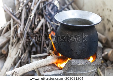 black pot boiling water for cooking on the fired stove next to firewood ...