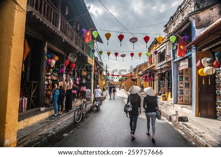 HOI AN, VIET NAM - FEBRUARY 4, 2015: Two unidentified asian female tourists in traditional vietnamese conical hats walk on a street in Hoi Ah on Feb 4, 2015. Hoi An is a World Heritage Site