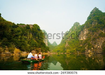 A touristic boat moves through a river between beautiful mountains of Trang An Grottoes, one of the main destinations in Ninh Binh Province, Vietnam