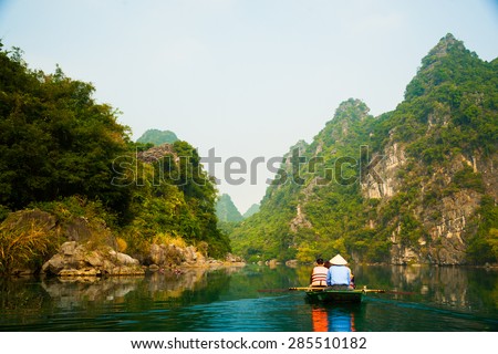 A touristic boat moves through a river between beautiful mountains of Trang An Grottoes, one of the main destinations in Ninh Binh Province, Vietnam