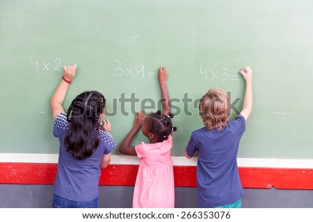 Mixed race school children writing on chalkboard.