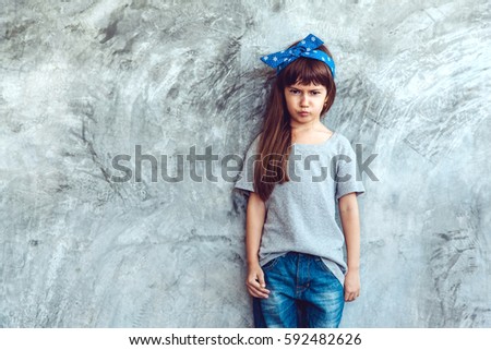 Fashion child wearing blank gray t-shirt and jeans posing against rough concrete wall, minimalist street fashion kids style