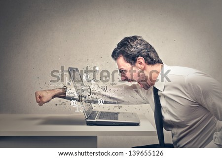 furious businessman throws a punch into the computer - stock photo