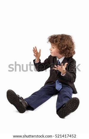 Little curly boy in a business suit sitting on the floor, screaming and gesturing with his hands. White background.