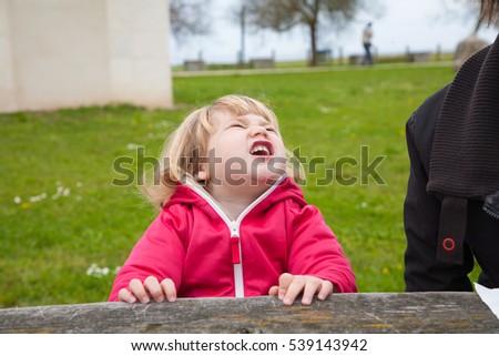 little blonde cute child sitting open mouth screaming and shouting expression face with green grass background