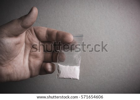 Mans hand holds plastic packet with cocaine powder or another drugs. Drug dealer selling drugs junkie
