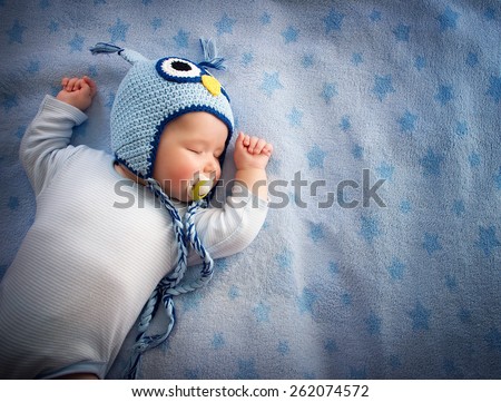 4 month old baby in owl hat sleeping on blue blanket