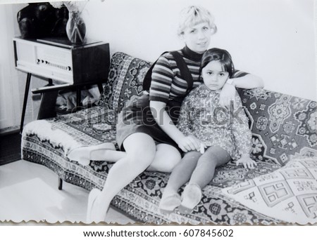 USSR, LENINGRAD - CIRCA 1973: Vintage photo of mom with daughter sitting on sofa in living room in Leningrad, USSR