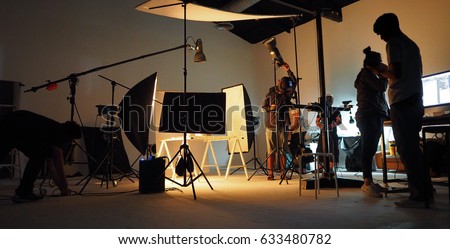 Behind the shooting production crew team and silhouette of camera and equipment in studio.