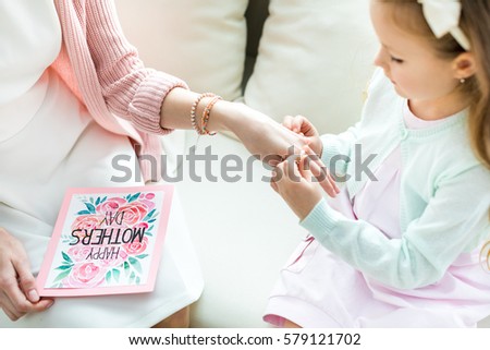 Partial view of cute little girl putting jewelry on hand of her mother on Mothers Day