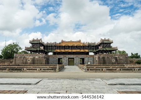 Walled fortress entrance to Hue Imperial City, Vietnam. Symmetrical frontal view with cobble stone ground and cloudy blue sky.