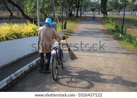 road sweeper worker with wooden broom tool pushing bicycle into a public park